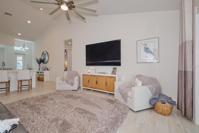 living room featuring ceiling fan with notable chandelier, light hardwood / wood-style flooring, and vaulted ceiling