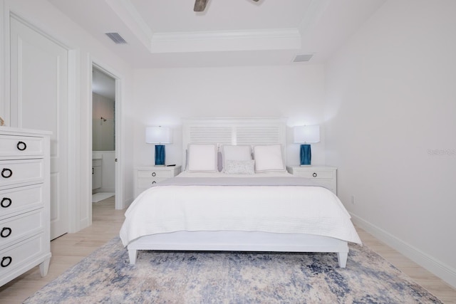 bedroom featuring light wood-type flooring, ensuite bath, ornamental molding, a tray ceiling, and ceiling fan