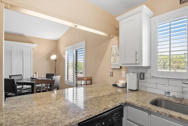 kitchen with white cabinetry, dishwasher, lofted ceiling, sink, and decorative backsplash