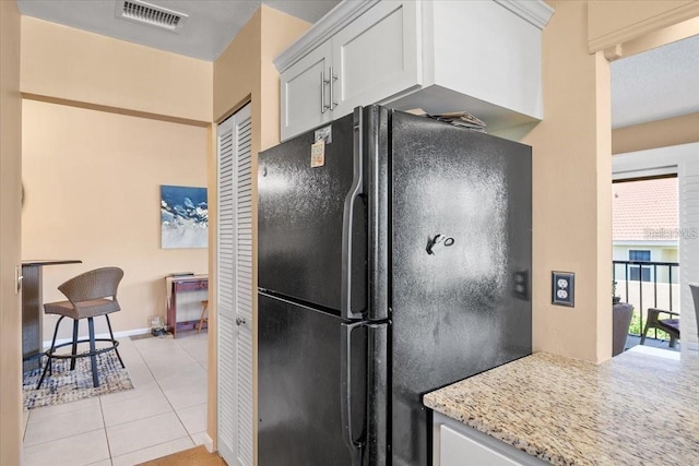 kitchen with black fridge, white cabinetry, light stone countertops, and light tile patterned floors