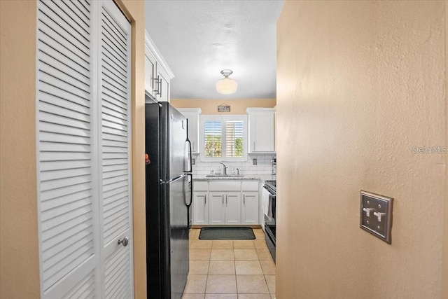 kitchen featuring white cabinetry, sink, tasteful backsplash, light tile patterned flooring, and black appliances