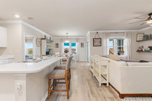 kitchen with ornamental molding, a center island with sink, white cabinets, light hardwood / wood-style floors, and hanging light fixtures