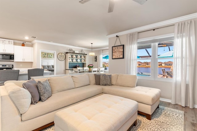 living room with ceiling fan, a water view, ornamental molding, and light wood-type flooring