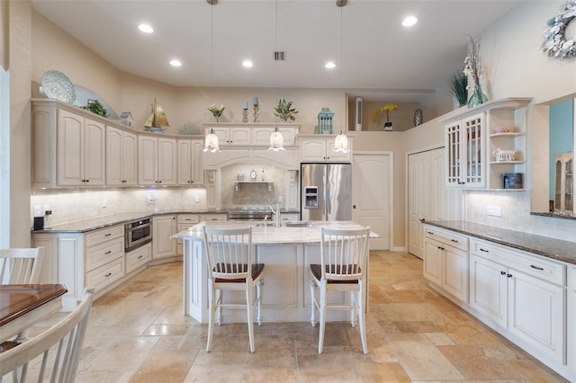 kitchen with a breakfast bar, stainless steel fridge, a center island with sink, and hanging light fixtures