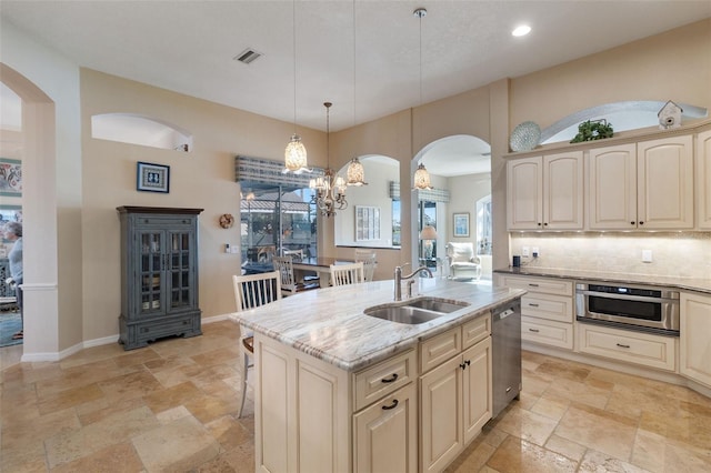 kitchen featuring sink, stainless steel appliances, light stone counters, an island with sink, and pendant lighting