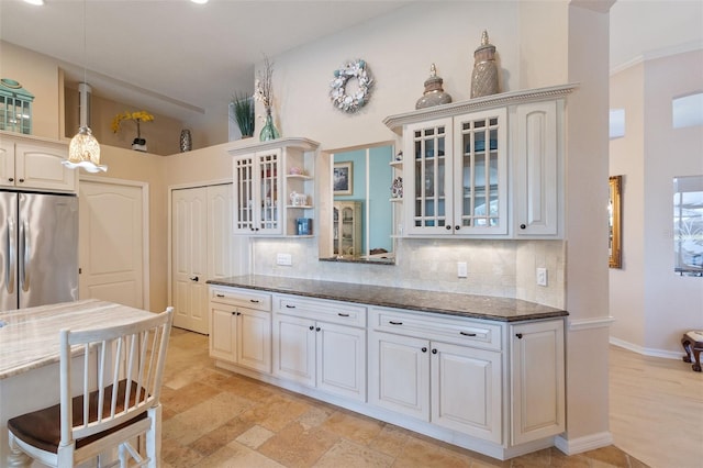 kitchen with stainless steel refrigerator, decorative backsplash, dark stone countertops, and white cabinets