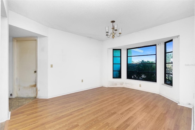 spare room with a notable chandelier, a textured ceiling, and light hardwood / wood-style flooring