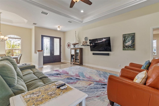 tiled living room featuring french doors, ceiling fan with notable chandelier, a raised ceiling, and ornamental molding