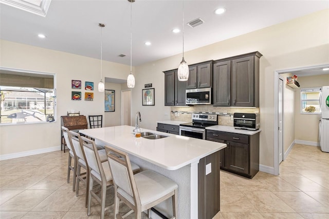 kitchen featuring appliances with stainless steel finishes, dark brown cabinets, sink, decorative light fixtures, and an island with sink