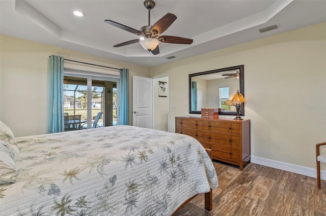 bedroom with ceiling fan, a raised ceiling, wood-type flooring, and access to outside