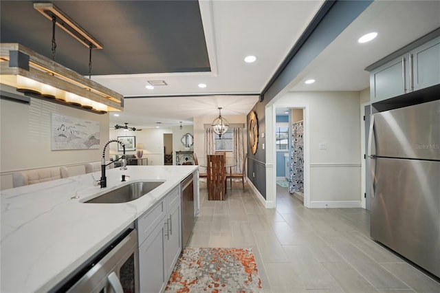 kitchen featuring light stone countertops, appliances with stainless steel finishes, sink, pendant lighting, and gray cabinets