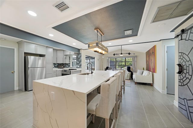 kitchen featuring light stone countertops, sink, a barn door, gray cabinets, and appliances with stainless steel finishes