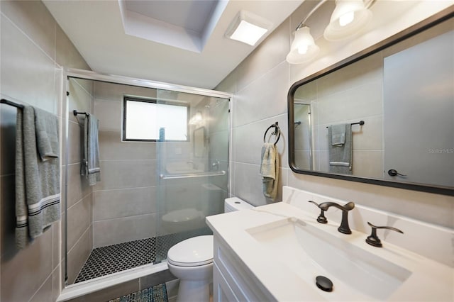 bathroom with vanity, toilet, a shower with door, and tile walls