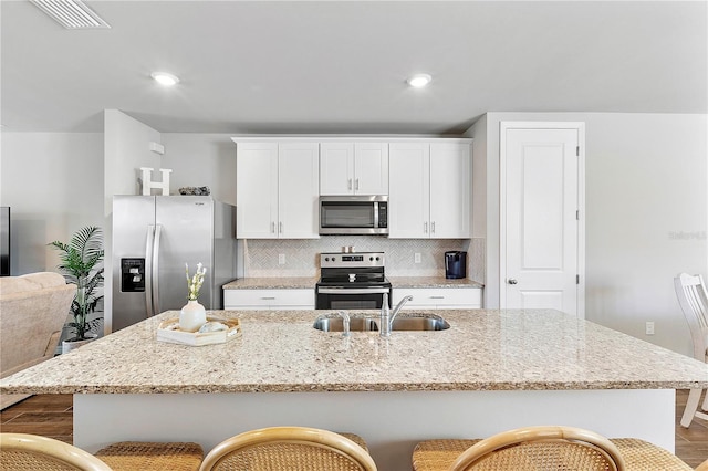 kitchen featuring a center island with sink, sink, decorative backsplash, appliances with stainless steel finishes, and a breakfast bar area