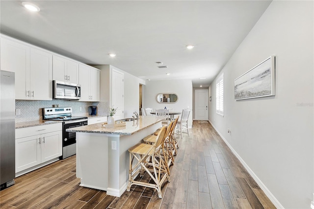 kitchen with sink, an island with sink, appliances with stainless steel finishes, a kitchen bar, and white cabinetry