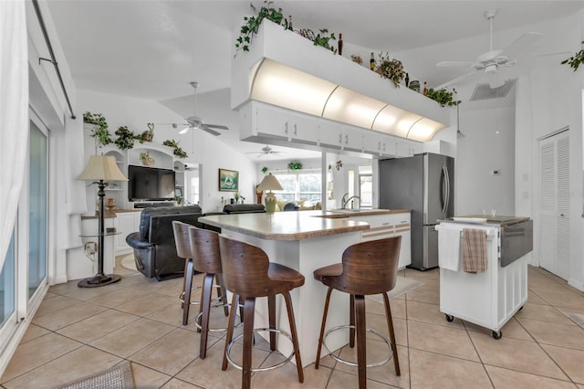 kitchen featuring stainless steel refrigerator, white cabinetry, a center island, and vaulted ceiling