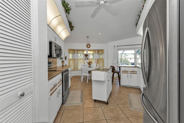 kitchen with ceiling fan with notable chandelier, stainless steel appliances, light tile patterned floors, decorative light fixtures, and white cabinetry