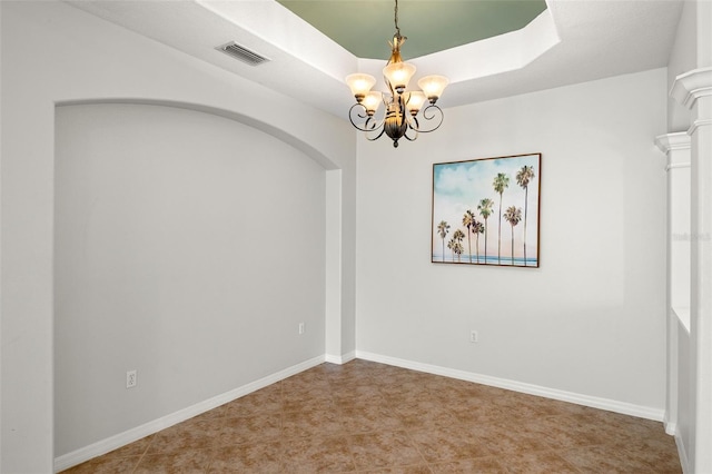 spare room with a tray ceiling, ornate columns, and an inviting chandelier