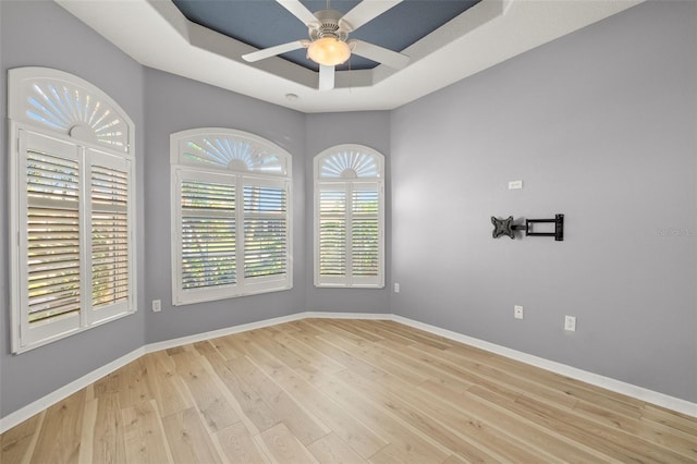 spare room with ceiling fan, light hardwood / wood-style floors, and a tray ceiling