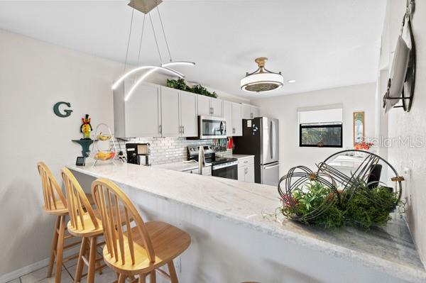 kitchen with a breakfast bar, white cabinetry, tasteful backsplash, kitchen peninsula, and stainless steel appliances