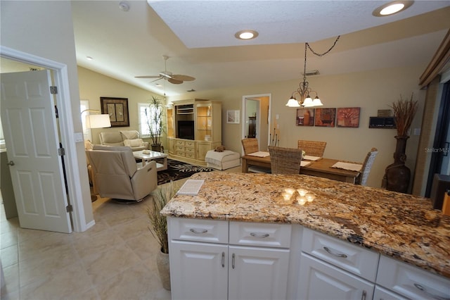 kitchen featuring light stone countertops, ceiling fan with notable chandelier, vaulted ceiling, decorative light fixtures, and white cabinetry