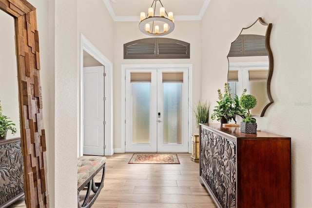 entrance foyer with french doors, crown molding, a chandelier, and light hardwood / wood-style floors