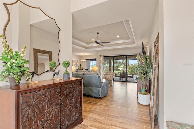 living room with ornamental molding, ceiling fan with notable chandelier, light hardwood / wood-style floors, and a tray ceiling