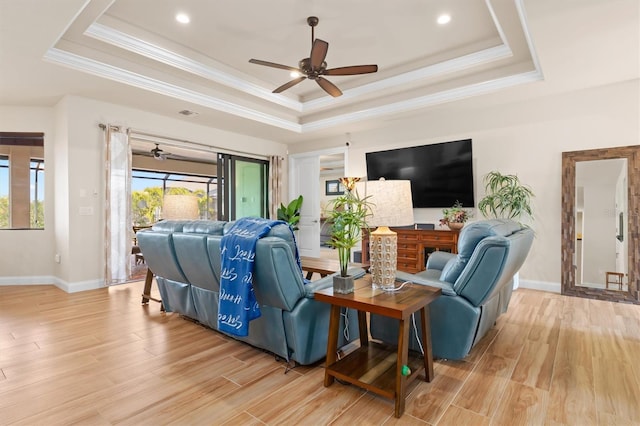 living room with crown molding, a raised ceiling, and light wood-type flooring