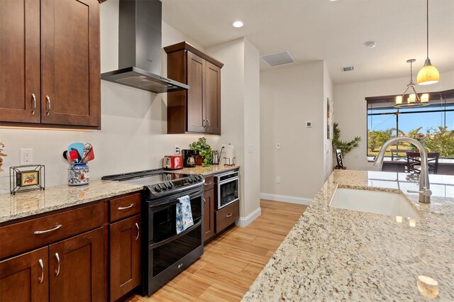 kitchen with sink, double oven range, light stone countertops, wall chimney exhaust hood, and light wood-type flooring