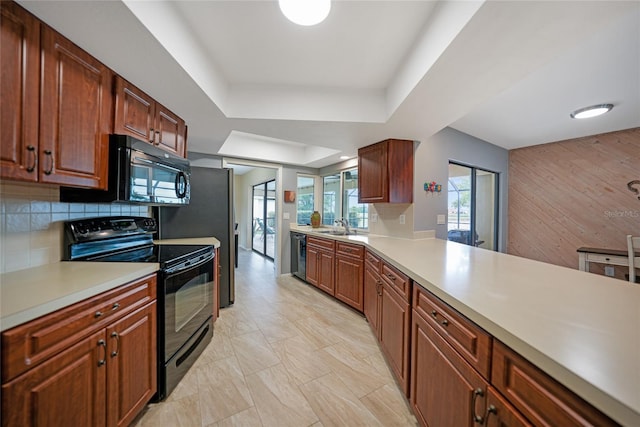 kitchen with kitchen peninsula, decorative backsplash, a raised ceiling, sink, and black appliances