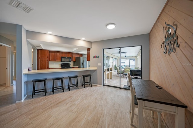 kitchen with ceiling fan, kitchen peninsula, wood walls, a kitchen bar, and black appliances