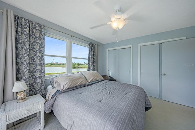 carpeted bedroom featuring multiple closets, ceiling fan, and a water view