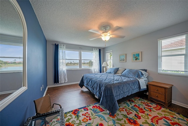 bedroom with a textured ceiling, a water view, ceiling fan, and dark hardwood / wood-style floors