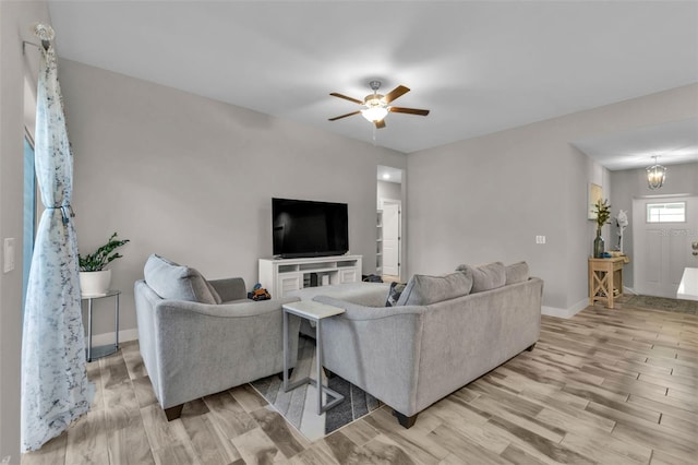 living room with ceiling fan with notable chandelier and light hardwood / wood-style flooring