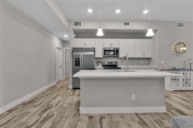 kitchen with appliances with stainless steel finishes, a kitchen island with sink, sink, pendant lighting, and white cabinets