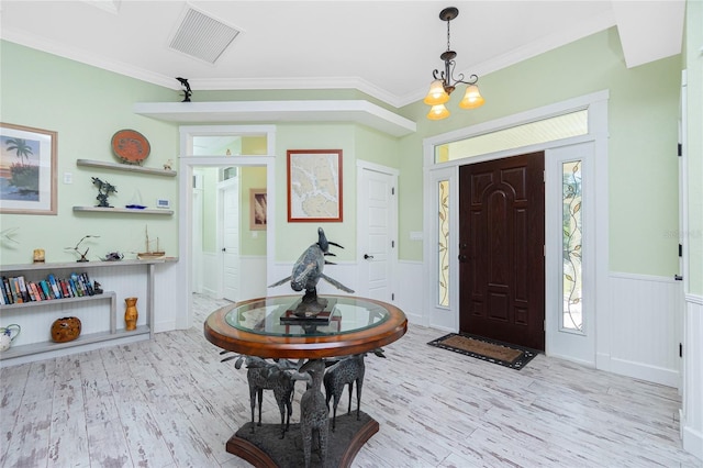 entrance foyer featuring light wood-type flooring, ornamental molding, and an inviting chandelier