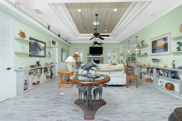 living room featuring a raised ceiling, crown molding, a healthy amount of sunlight, and a stone fireplace