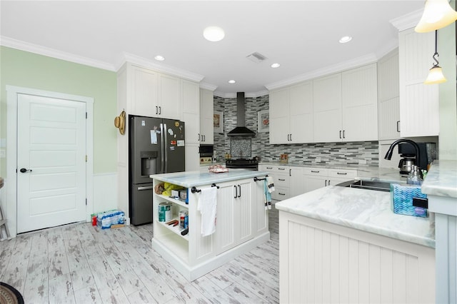 kitchen featuring hanging light fixtures, ornamental molding, wall chimney exhaust hood, stainless steel refrigerator with ice dispenser, and white cabinetry