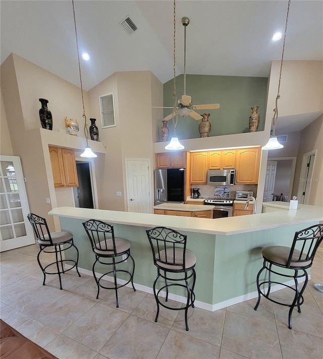 kitchen with appliances with stainless steel finishes, light brown cabinets, tasteful backsplash, and high vaulted ceiling