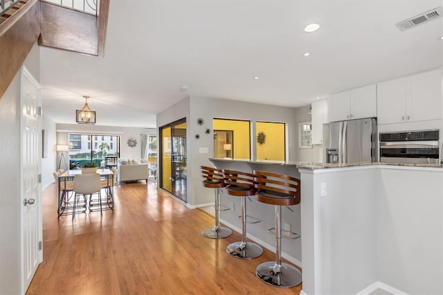 kitchen featuring light stone countertops, appliances with stainless steel finishes, a breakfast bar, light hardwood / wood-style floors, and white cabinetry