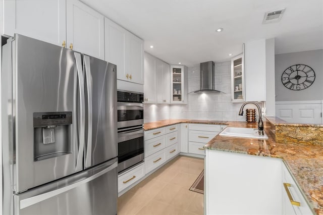 kitchen with light stone countertops, white cabinetry, sink, stainless steel appliances, and wall chimney range hood