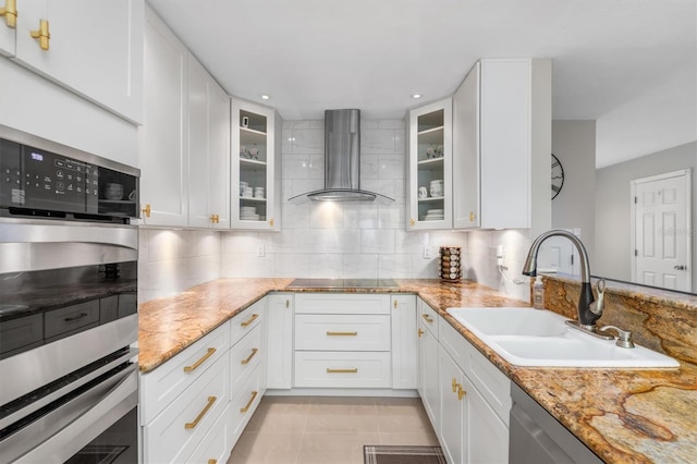 kitchen with light stone countertops, appliances with stainless steel finishes, wall chimney exhaust hood, sink, and white cabinetry