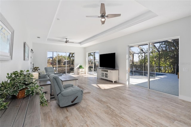 living room with ceiling fan, light hardwood / wood-style floors, a wealth of natural light, and a raised ceiling