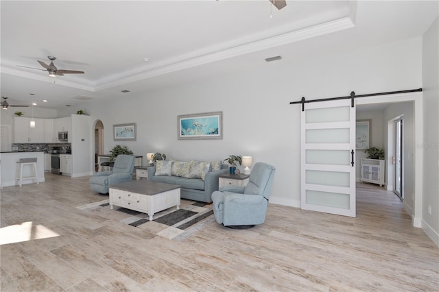 living room featuring ceiling fan, a raised ceiling, a barn door, and light wood-type flooring