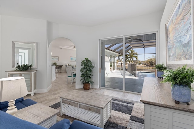 living area featuring a sunroom, light wood-style flooring, arched walkways, and baseboards