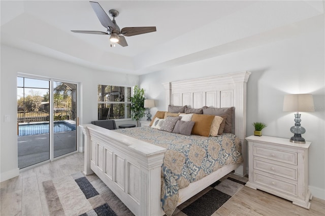 bedroom featuring a tray ceiling, light wood finished floors, a ceiling fan, access to outside, and baseboards