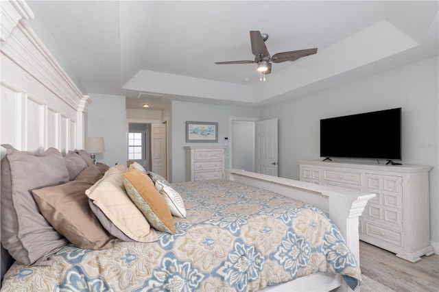 bedroom featuring ceiling fan, light wood-type flooring, and a tray ceiling