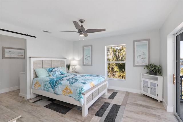 bedroom featuring ceiling fan, a barn door, wood finished floors, visible vents, and baseboards