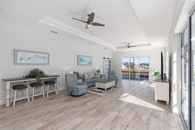 living room with a raised ceiling, visible vents, a barn door, ceiling fan, and wood finished floors