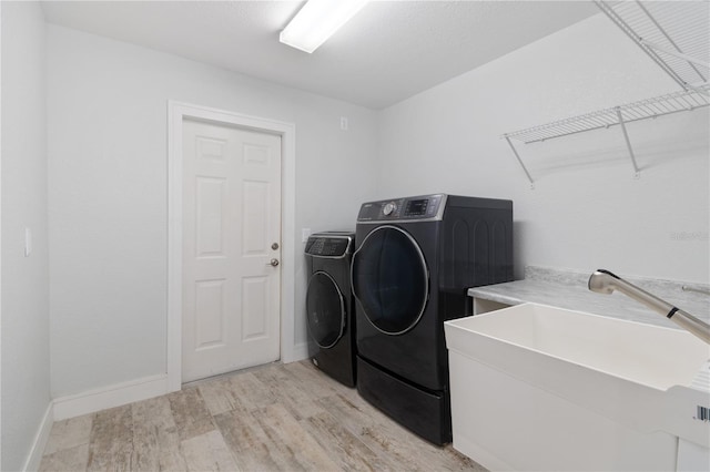 clothes washing area with laundry area, light wood finished floors, baseboards, separate washer and dryer, and a sink